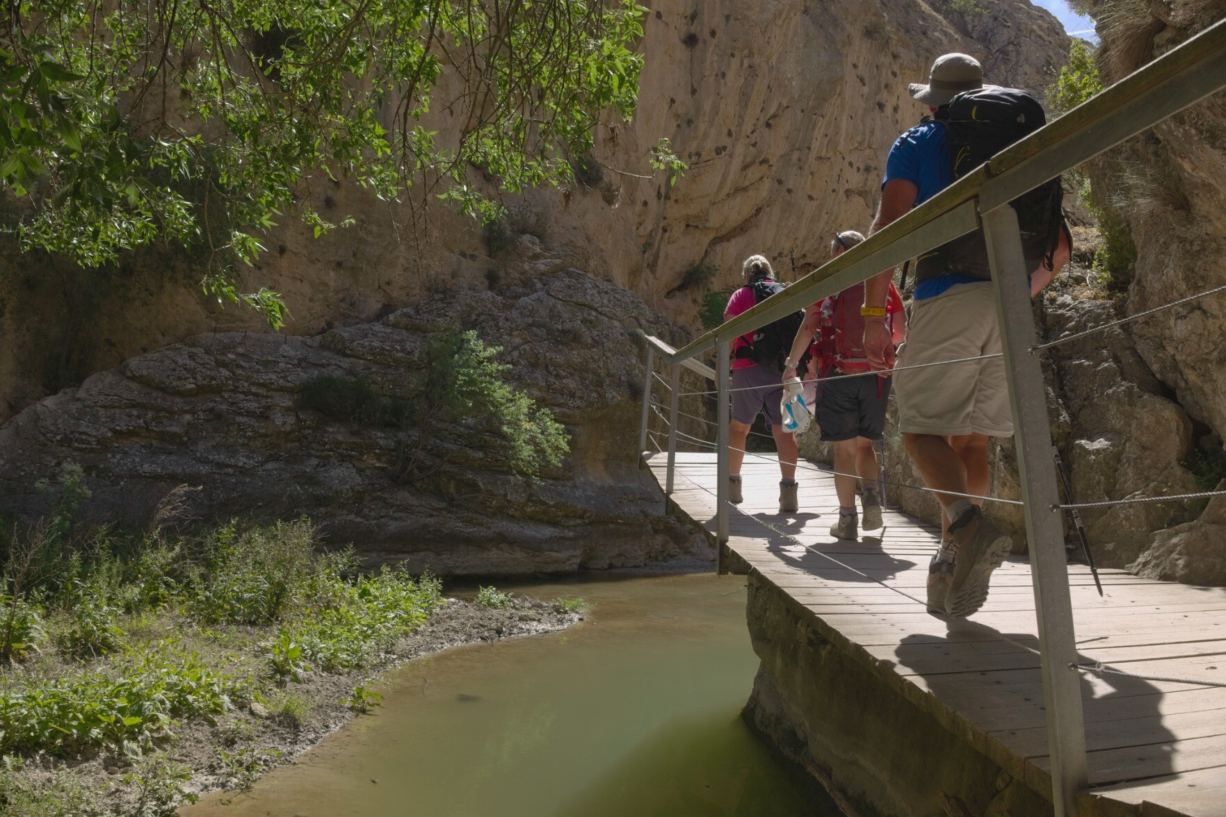 3 hikers cross a exposed walkway above a river with steep sided walls