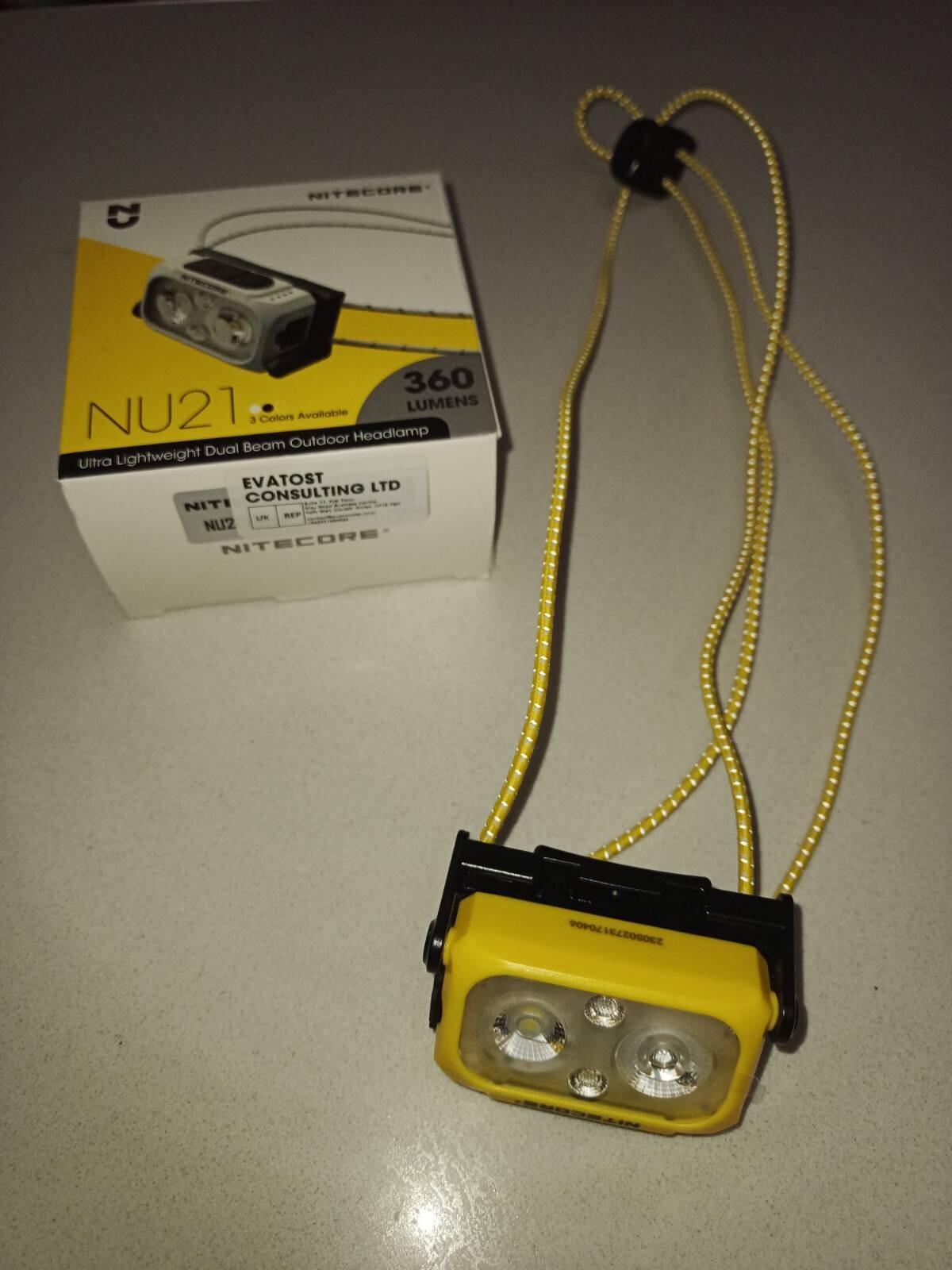 A yellow head torch with cord bands lays next to a yellow and white NU21 box