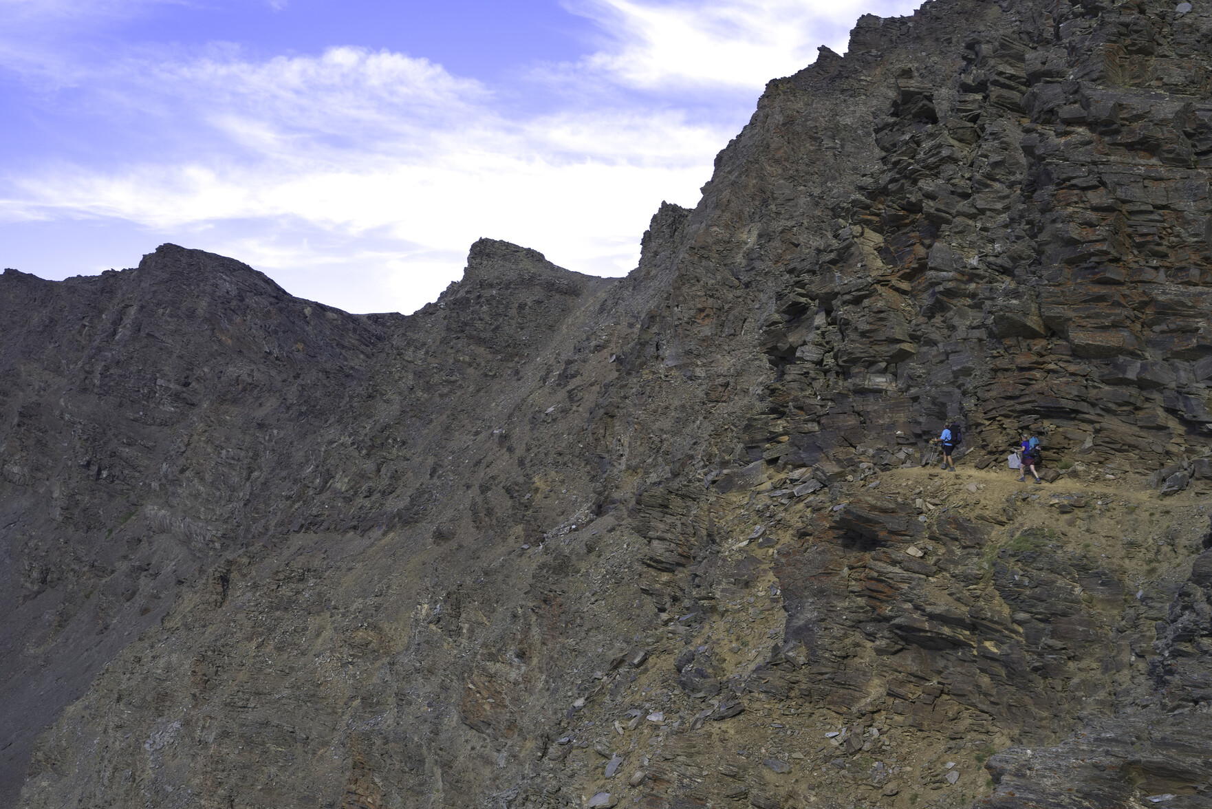 Some hikers walk along a narrow ledge across a mountain face