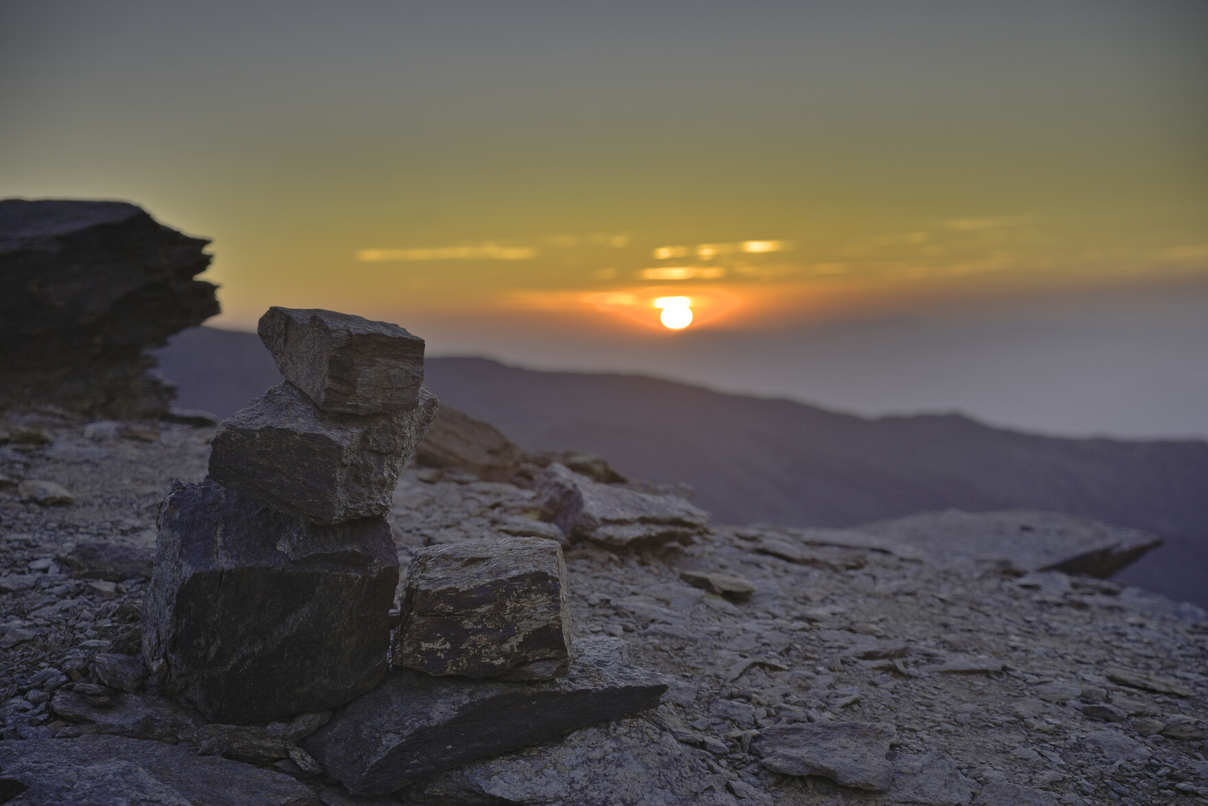 A large cairn is in the foreground whilst the sun sets in the background