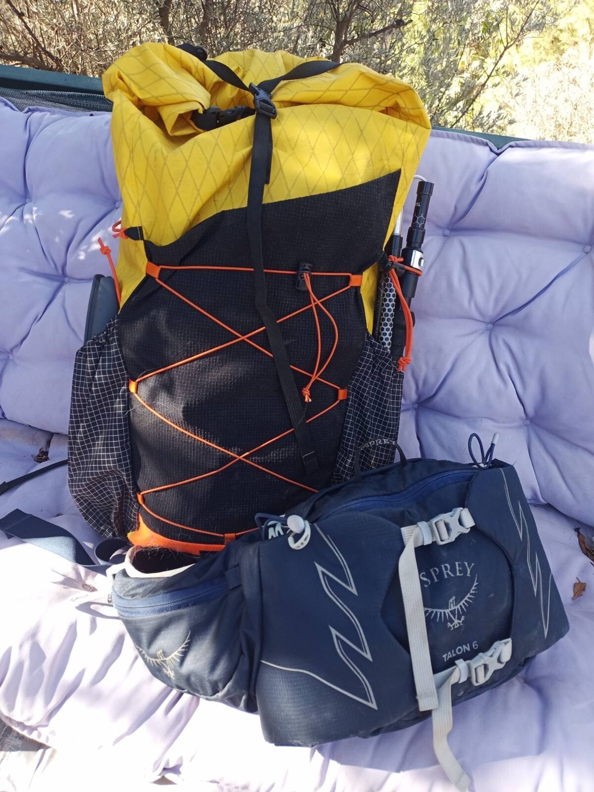 A yellow and black Atom pack rucksack sits next to a blue Osprey waist pack