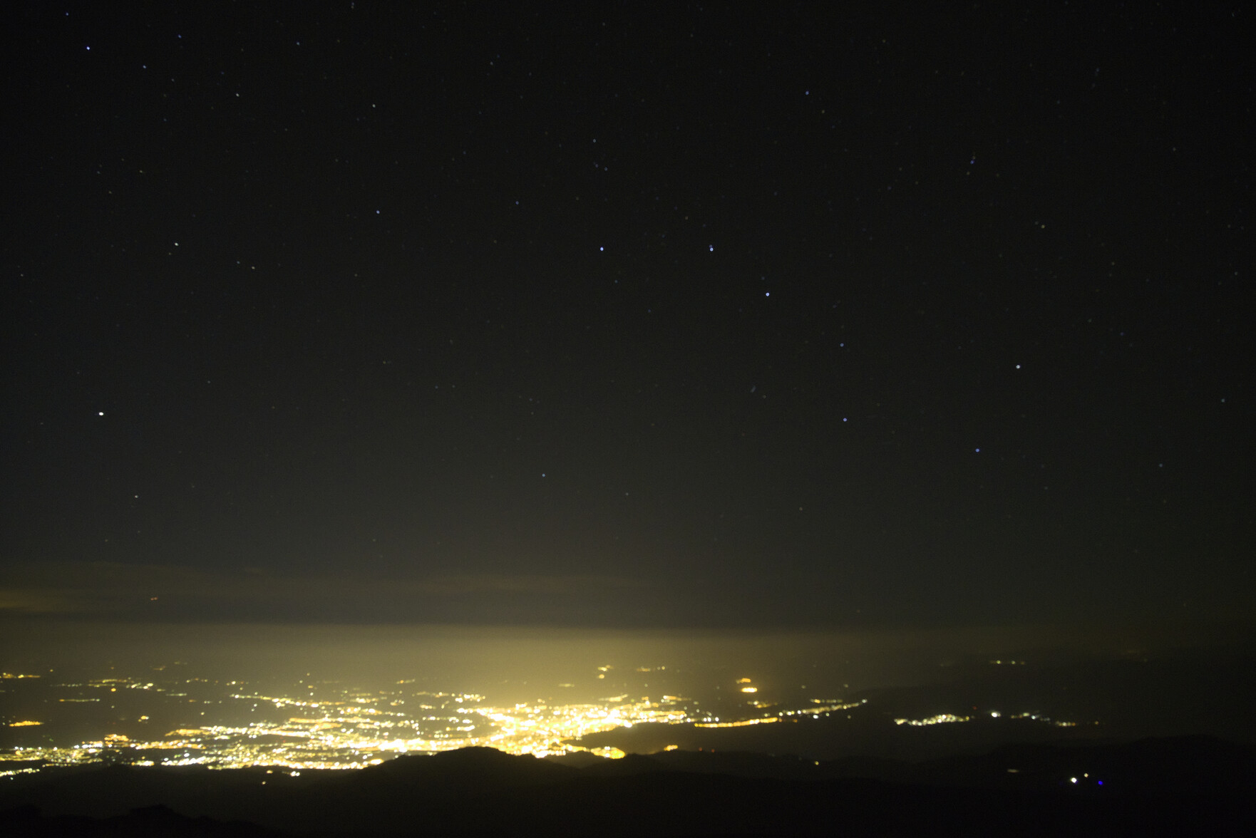The lights from the city of Granada, Spain are at the bottom of the image. Above, clear skies and stars