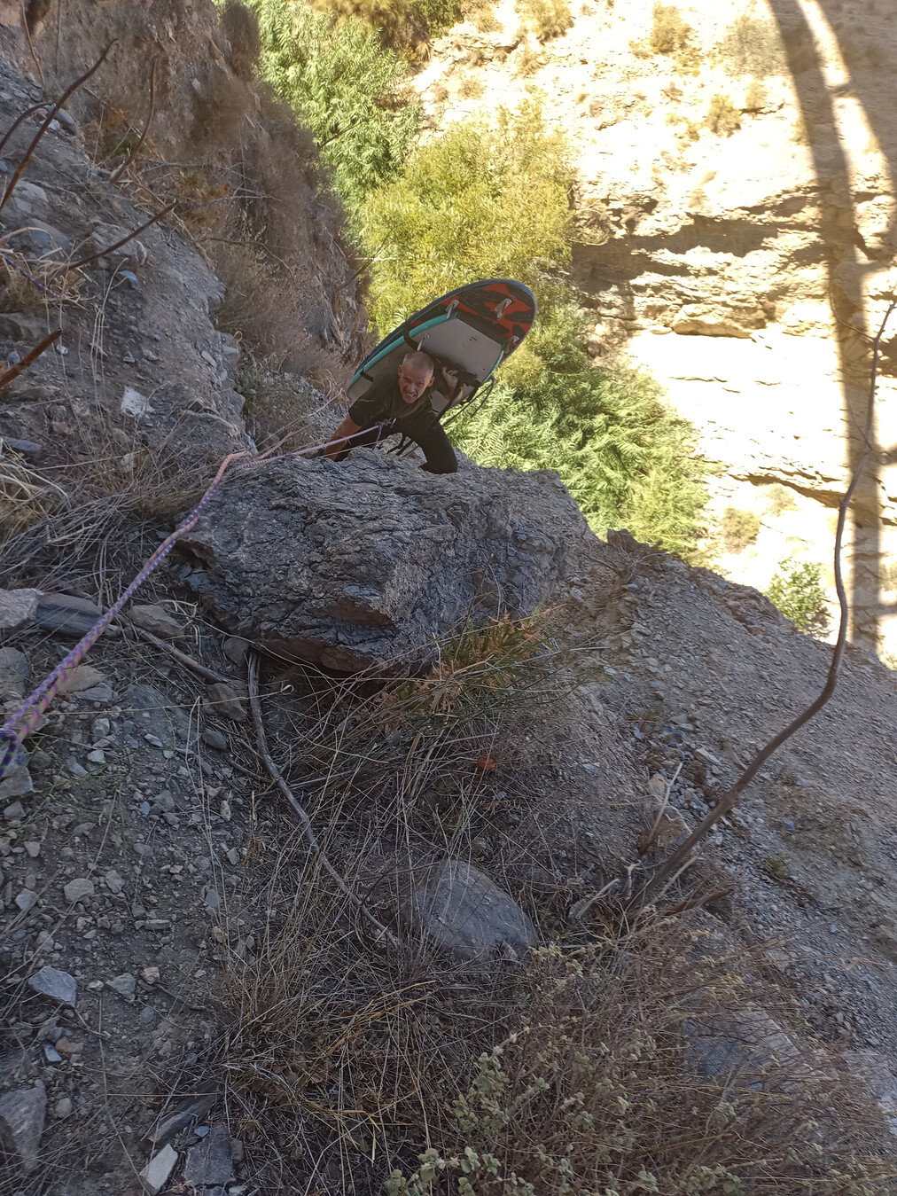 Ropes belay a person on a steep slope carrying surfboards