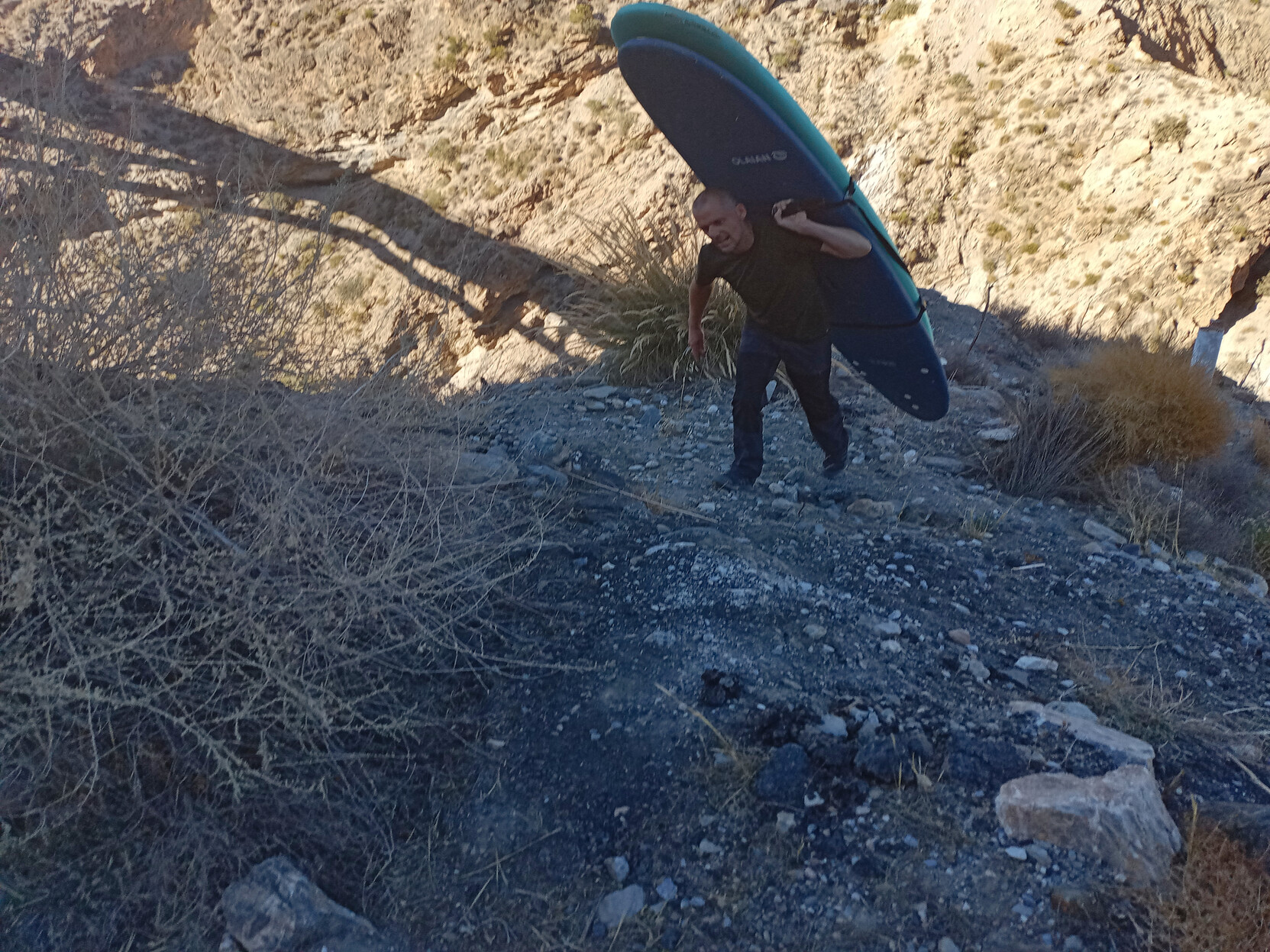 A surfboard is being carried across a steep scree slope