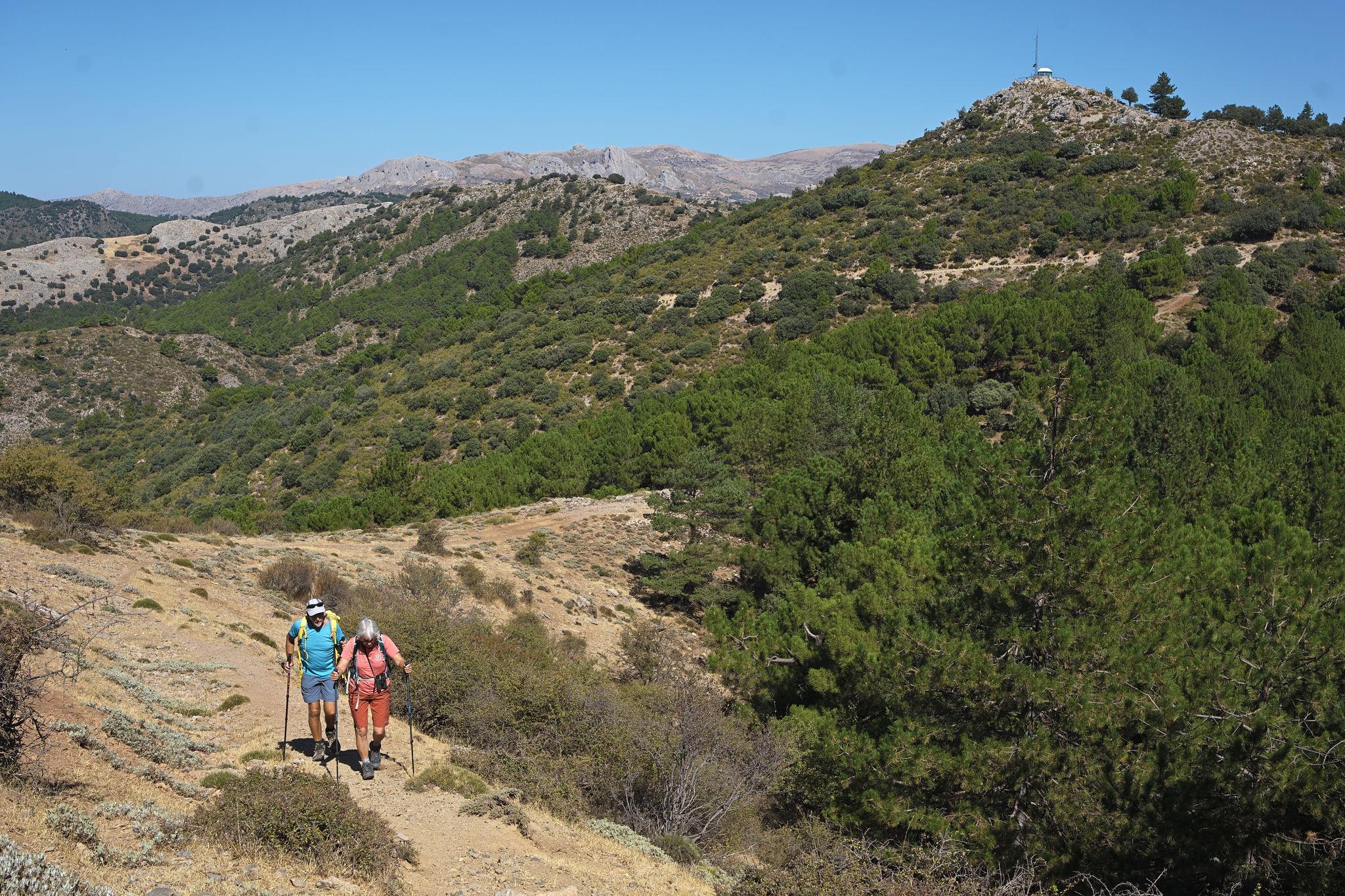 Two people pass along a track. Above rises the peak of Cerro Toriles and it's fire lookout